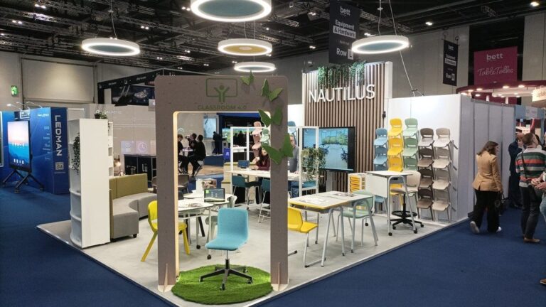 Stand de exposi&ccedil;&atilde;o com mesas, cadeiras de v&aacute;rias cores, plantas e um painel Classroom 4.0.