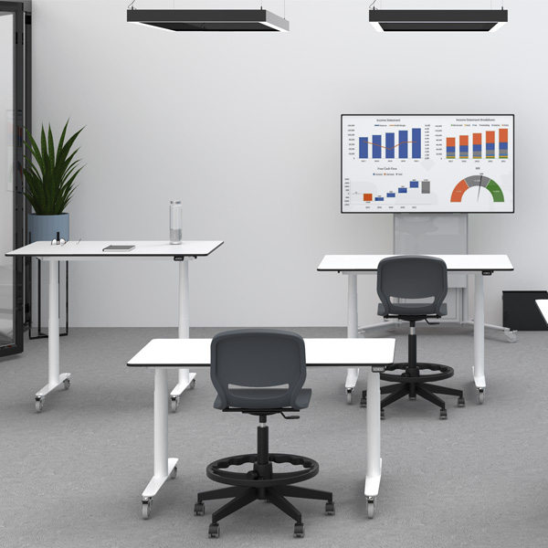 Espaço com mesas Flow, cadeiras, planta e ecrã com gráficos.