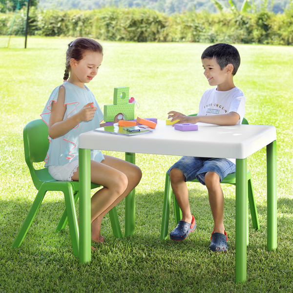 Duas crianças brincam com blocos de construção numa mesa branca ao ar livre, sentadas em cadeiras verdes.