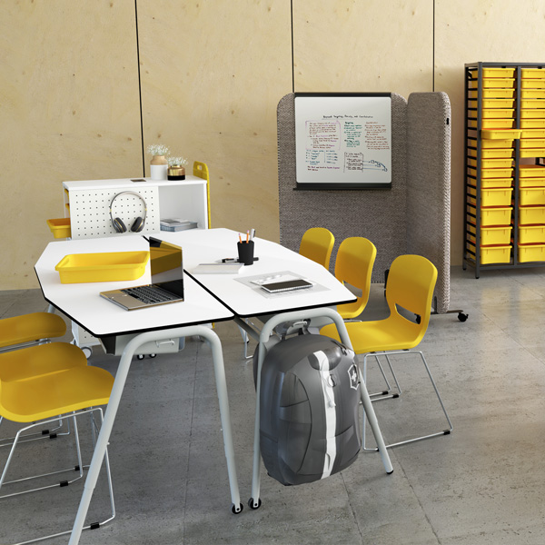 Sala de aula com mesas brancas, cadeiras amarelas, dispositivos digitais e quadro com anotações.