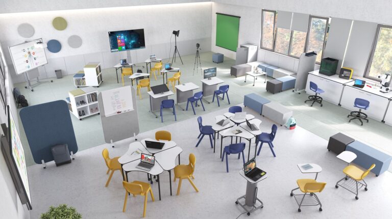 Sala de aula com mesas e cadeiras de várias cores, computadores portáteis, quadros, estantes e equipamentos.