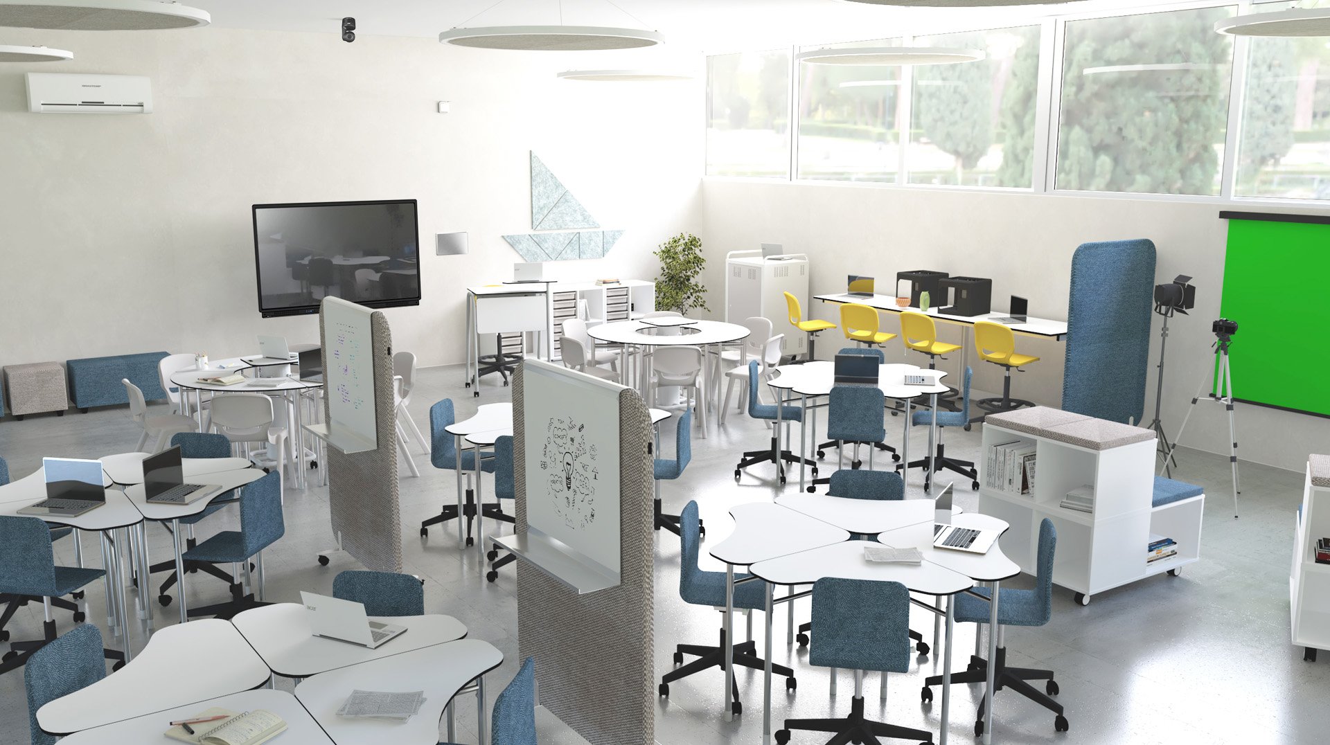 Sala de aula com mesas brancas agrupadas, cadeiras azuis e amarelas, computadores, fundo verde e câmara em tripé.
