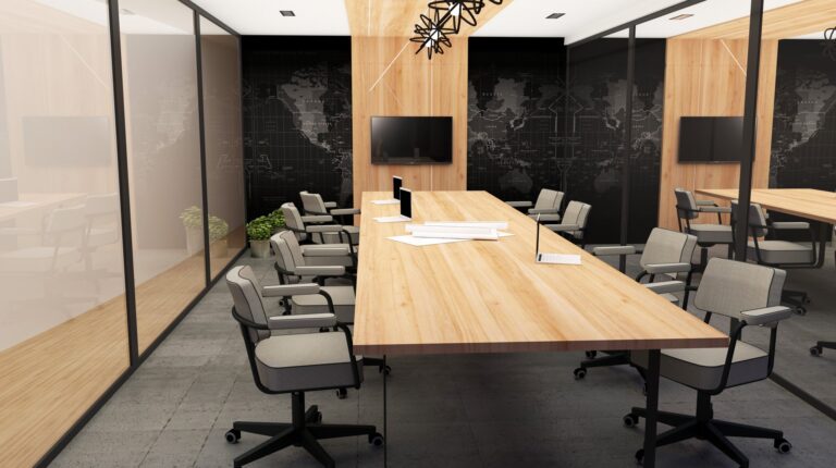 Sala de reuniões com mesa comprida de madeira, cadeiras cinzentas, ecrãs e mapa-múndi na parede.