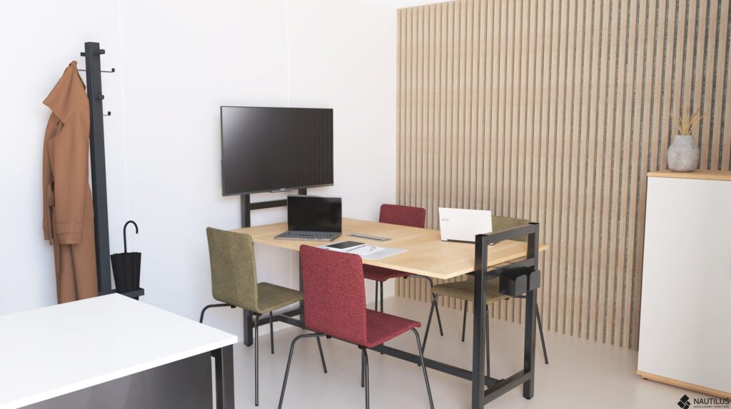 Sala com mesa de madeira, cadeiras de várias cores, computadores portáteis, ecrã e bengaleiro.