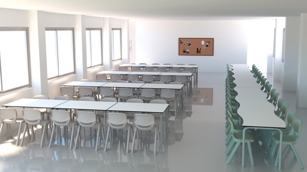 Sala com mesas e cadeiras brancas em filas e painel de cortiça com fotografias na parede.