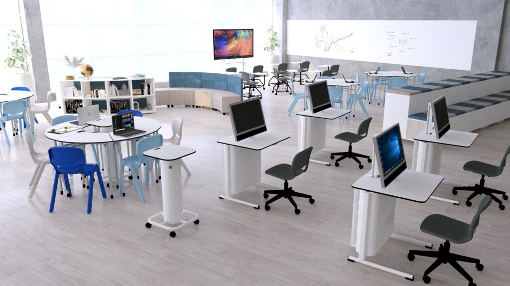 Sala com mesas de diferentes alturas, cadeiras com rodas, sofá, computadores e quadros de escrita.