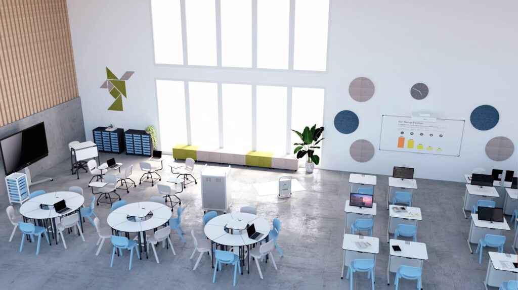 Sala com mesas redondas e rectangulares, cadeiras brancas e azuis, computadores portáteis e ecrãs.