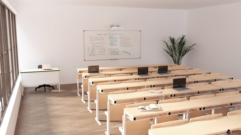 Sala de aula com mesas de madeira em filas, computadores portáteis e quadro com anotações.