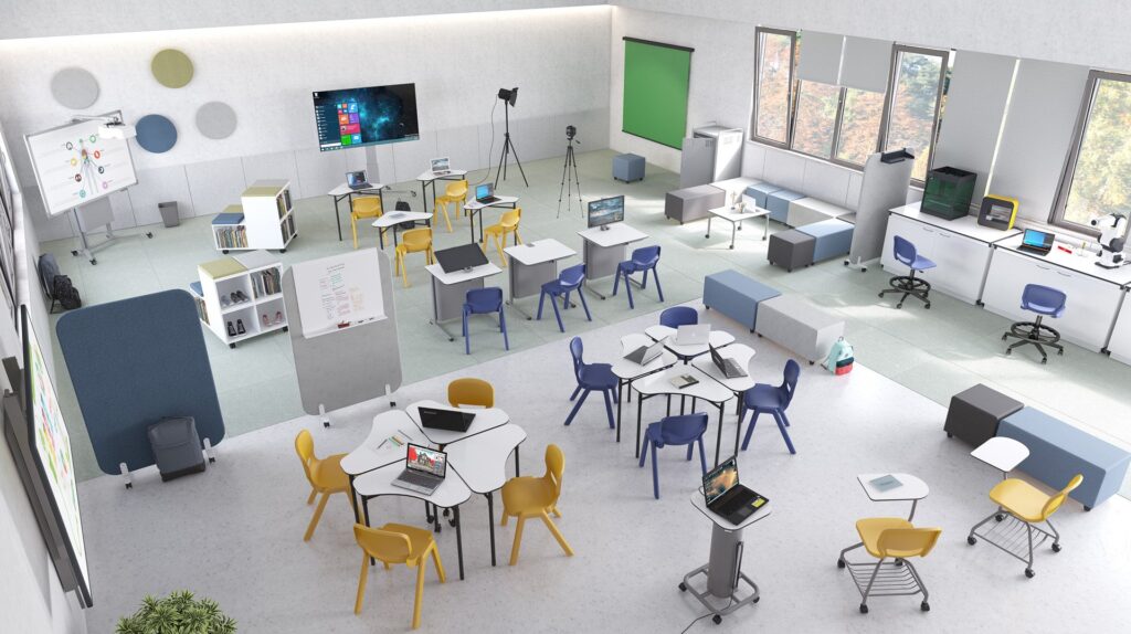 Sala de aula com mesas, cadeiras de várias cores, computadores portáteis, estantes e equipamentos.