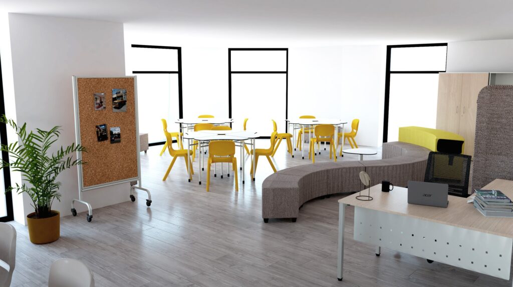 Sala com cadeiras amarelas, mesas redondas, painel de cortiça e zona de assentos curvos cinzentos.