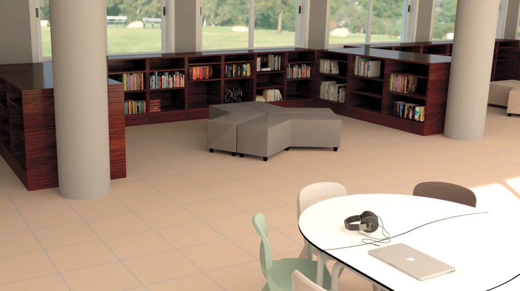Biblioteca com estantes de madeira e mesa redonda com computador portátil e auscultadores, rodeada de cadeiras de várias cores.