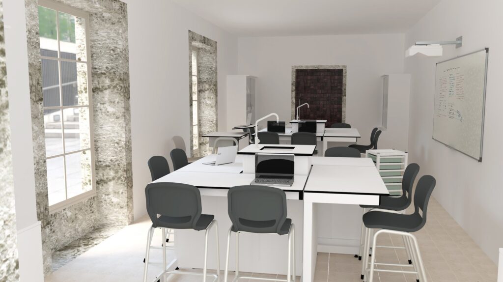 Sala com mesas altas, cadeiras cinzentas, computadores portáteis e quadro branco.