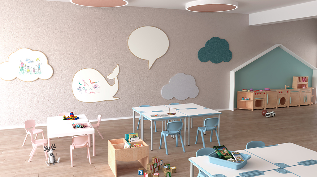 Sala infantil com mesas e cadeiras em tons pastel, cozinha de brincar e painéis em forma de nuvem e baleia.