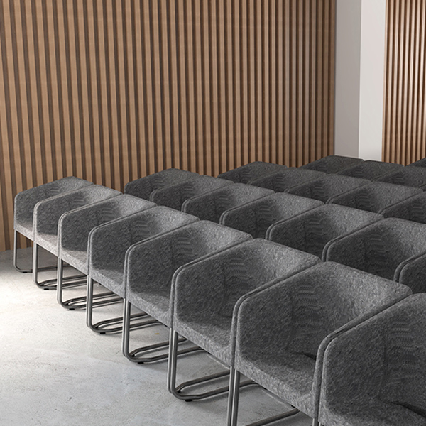 Cadeiras cinzentas dispostas em filas numa sala com parede revestida a ripas de madeira.