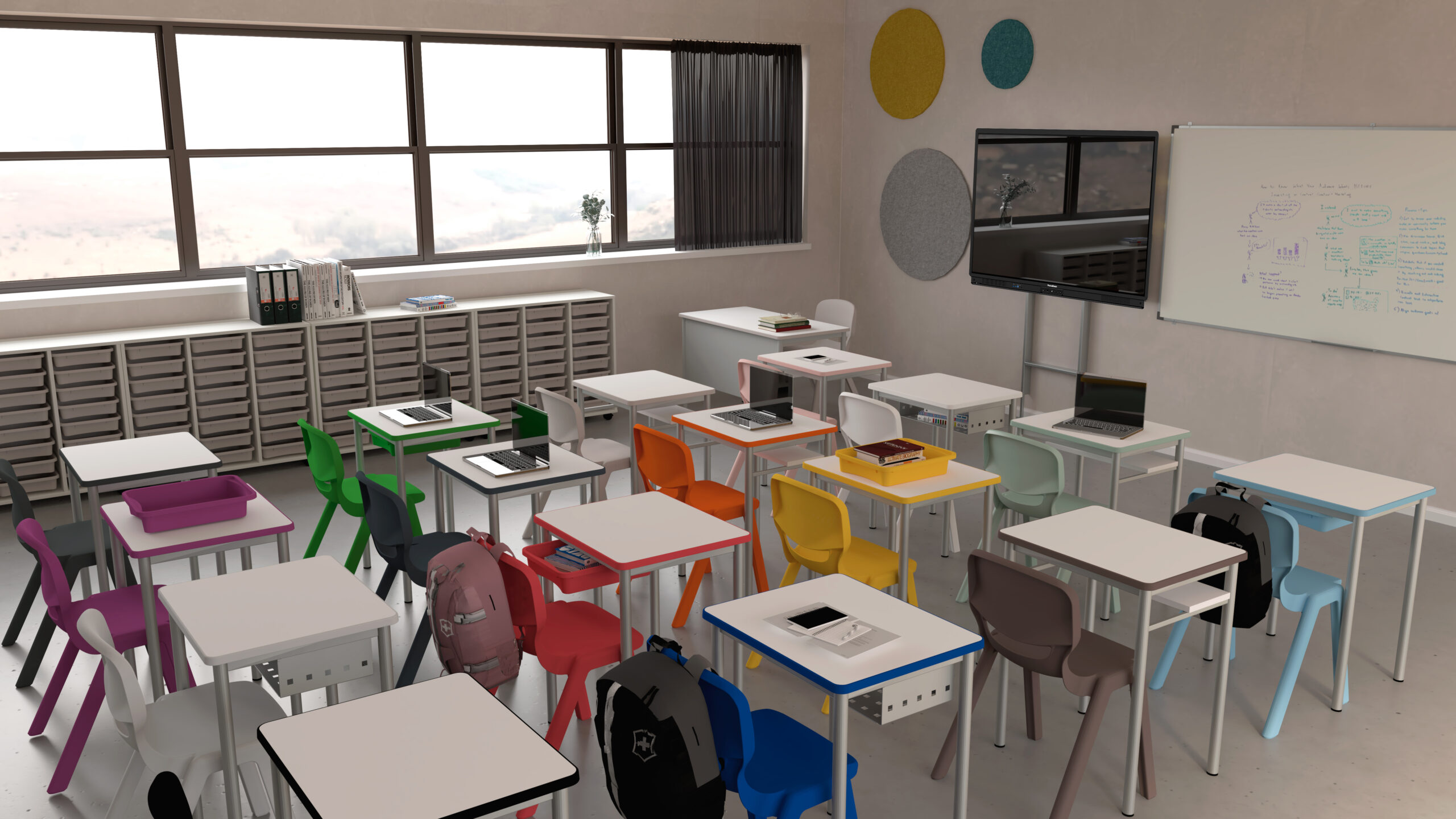 Sala de aula com mesas brancas, cadeiras de várias cores, computadores portáteis, quadro e ecrãs.