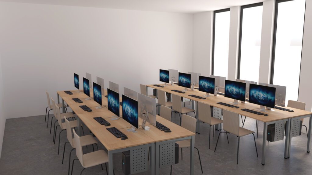 Sala de informática com mesas de madeira em filas, monitores, teclados e cadeiras.
