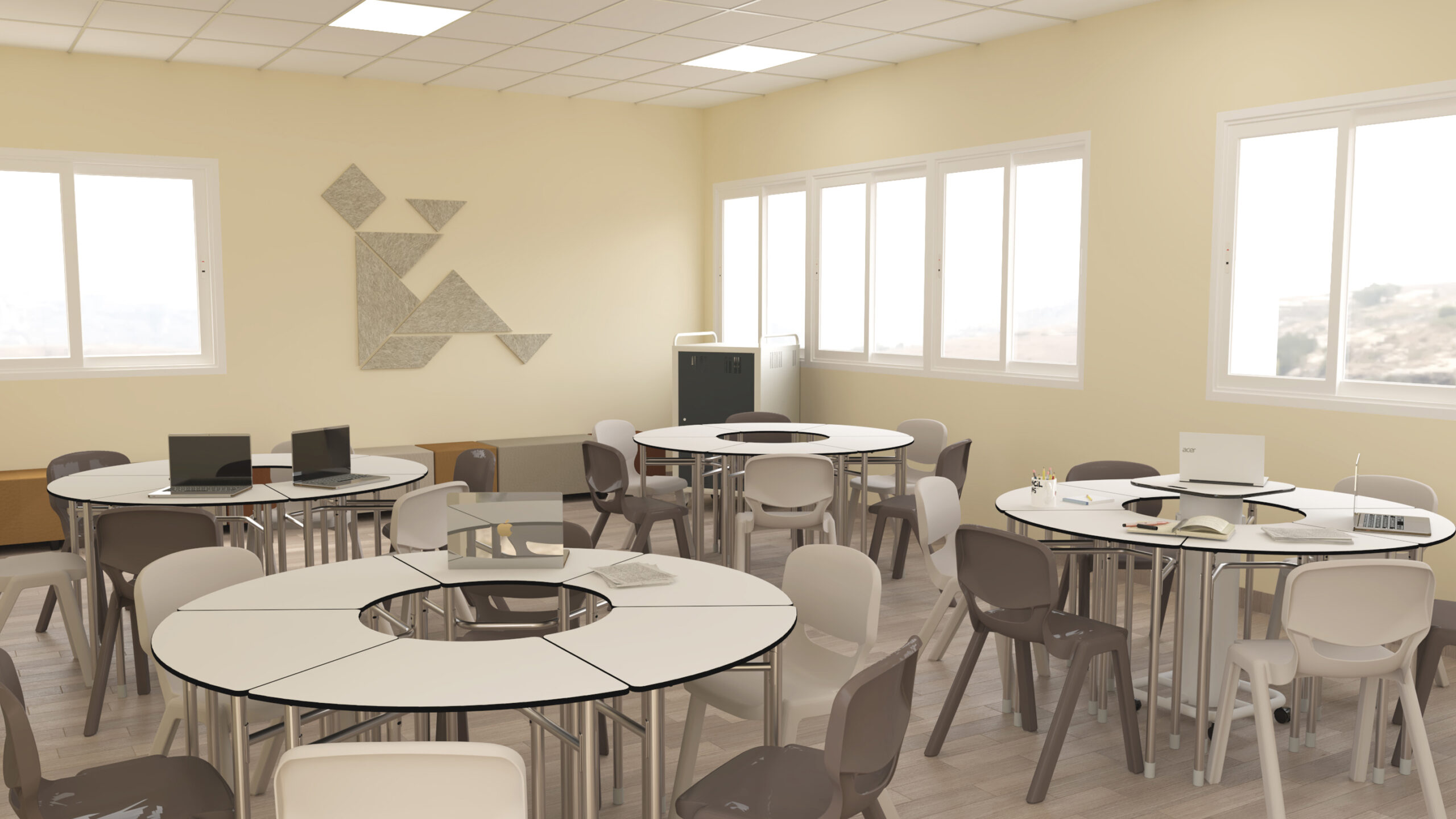Sala com mesas redondas, cadeiras cinzentas, computadores portáteis e livros.