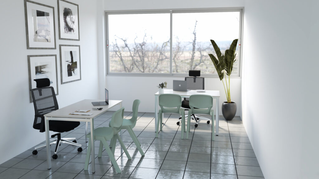 Espaço de trabalho com mesas, cadeiras, computadores portáteis e planta junto à janela.