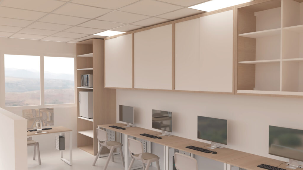 Sala de informática com mesas, cadeiras, monitores e arrumação junto às paredes.