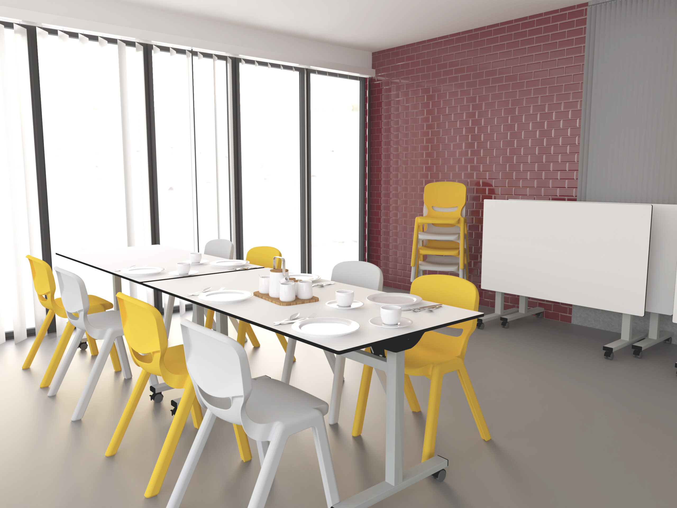 Un comedor moderno con dos mesas dispuestas para comer, rodeadas de sillas amarillas y blancas. Grandes ventanales dejan entrar la luz natural y al fondo se ve una pared de ladrillo rojo. En la esquina hay mesas plegadas y sillas apiladas.