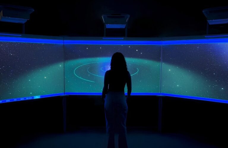 Pessoa diante de uma parede curva de projec&ccedil;&atilde;o com imagens luminosas em tons de azul e verde.